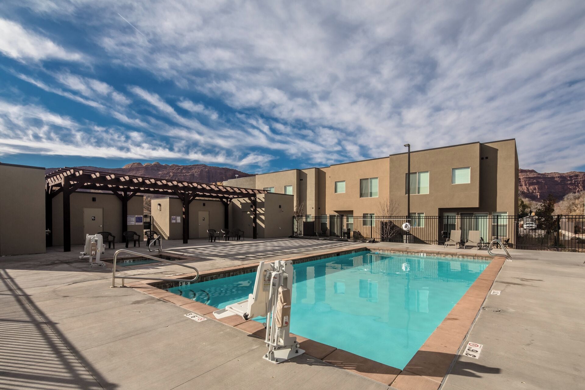 A swimming pool with a pergola, a covered seating area, and a mountain backdrop.