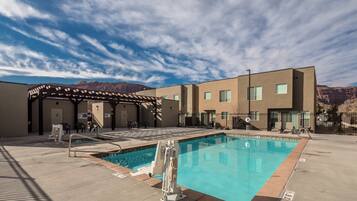 A swimming pool with a pergola, a covered seating area, and a mountain backdrop.