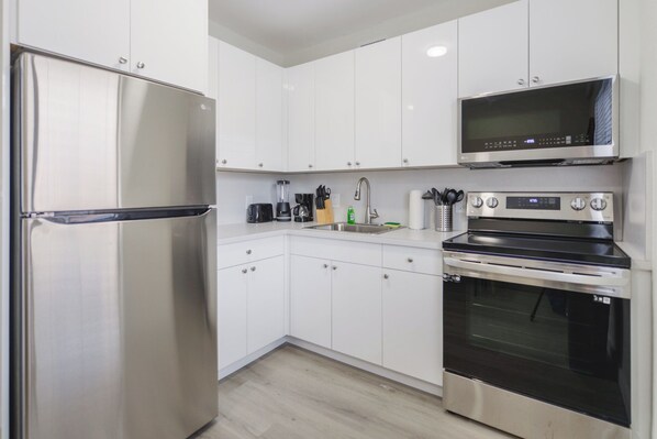 A modern kitchen with stainless steel appliances, white cabinetry, and a built-in microwave. - Little Havana Stay - We Host (Miami)
