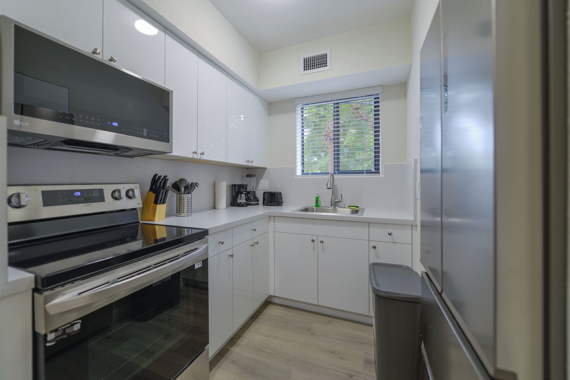 Una cocina moderna con armarios blancos, electrodomésticos de acero inoxidable y una ventana con persianas.