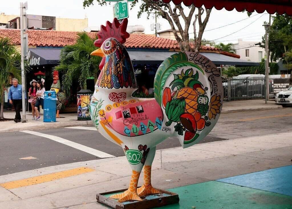 Eine farbenfrohe Hahn-Statue mit kubanischen Dekorationen, darunter eine Ananas und ein Schild mit der Aufschrift 'Little Havana.'