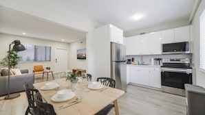 Una cucina moderna con mobili bianchi, elettrodomestici in acciaio inossidabile e un'area pranzo con tavolo e sedie in legno.