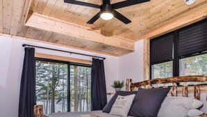 Ein Schlafzimmer mit hölzernem Kopfteil, einem Bett mit gestreifter Bettwäsche, einem Deckenventilator und großen Fenstern mit Vorhängen.