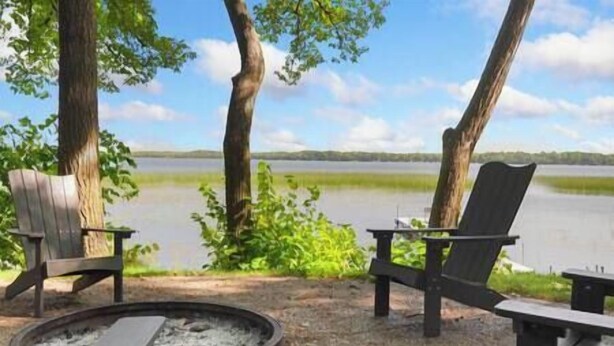 Un espacio de estar junto al lago con dos sillas Adirondack y un brasero.