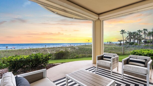 A covered outdoor seating area with a view of the beach and ocean at sunset. - Beach Colony West 1C (Pensacola)