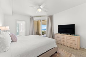 Ein Schlafzimmer mit Bett, Fernseher auf einer Holzkommode und Blick ins Freie durch eine Tür.