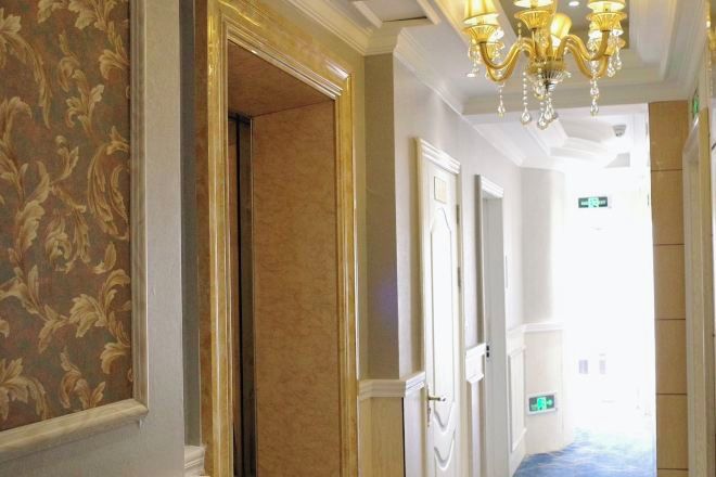 A hallway with patterned wallpaper, a chandelier, and doors leading to other rooms.
