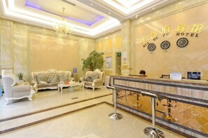 Egy szállodai előcsarnok, amelyben recepció, ülősarok és egy impozáns csillár található.