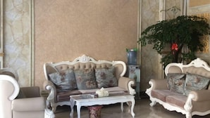 Une pièce avec un canapé beige agrémenté de coussins à motifs floraux, une table basse blanche et une grande plante verte.