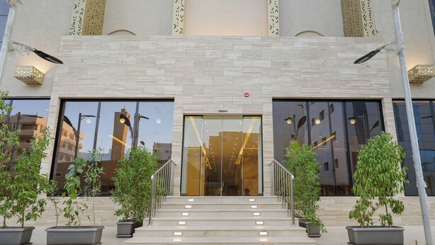 A modern building with a glass entrance, steps leading up to it, and potted plants on either side. - karam suite (Riyadh)