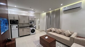A modern living room with a beige sofa, a coffee table, and a TV mounted on the wall. - karam suite (Riyadh)