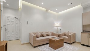 A modern living room with a beige sofa, a wooden coffee table, and a lamp. - karam suite (Riyadh)