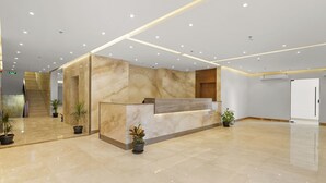 A modern reception area with a marble reception desk, potted plants, and a staircase in the background. - karam suite (Riyadh)