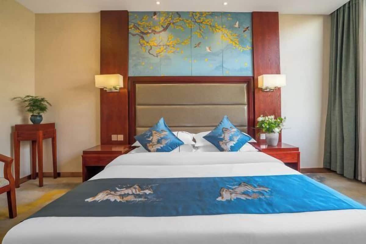 A hotel room with a large bed, two nightstands, a wooden headboard, and a wall mural.