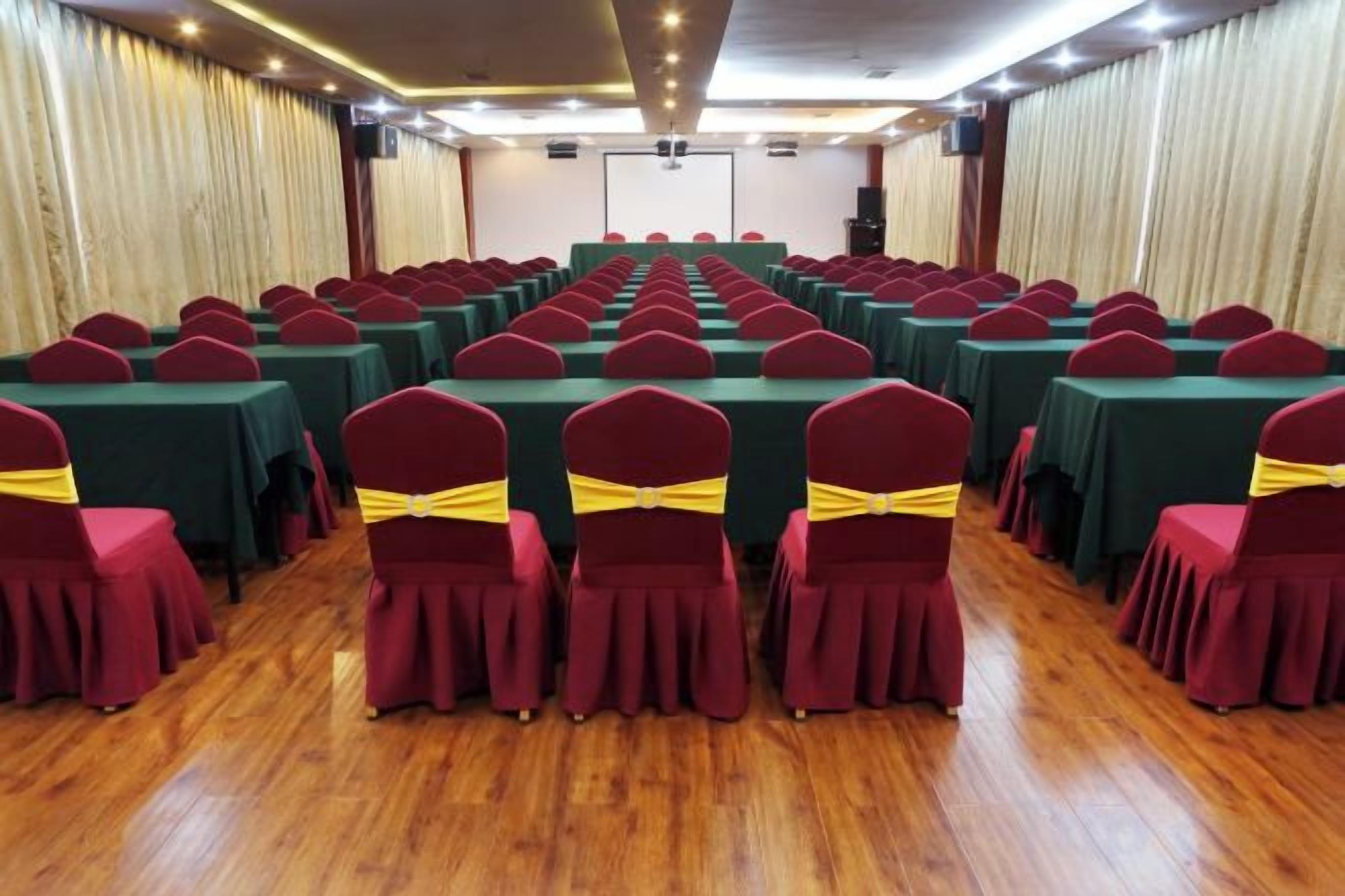 A conference room with rows of tables and chairs, a stage at the front, and curtains on the sides.