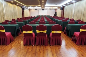 Un salón de conferencias con filas de mesas y sillas, un escenario al frente y cortinas a los lados.