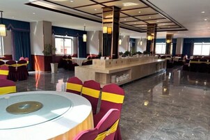 Un amplio vestíbulo de hotel con una zona de bar central, mesas redondas y sillas con amarres amarillos.