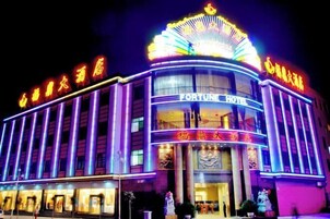 Un hotel con un letrero llamativo que dice "FORTUNE HOTEL" y letreros de neón iluminados sobre la entrada.