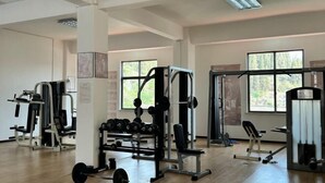 A gym with weightlifting equipment, large windows, and a wooden floor. - Fortune Hotel (Luxi)