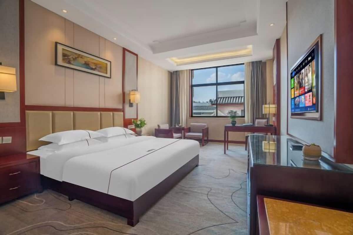 A hotel room with a large bed, a desk, a chair, and a TV.