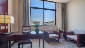 A hotel room with a large window, a desk with a chair, a small table with a plant, and two armchairs. - Fortune Hotel (Luxi)