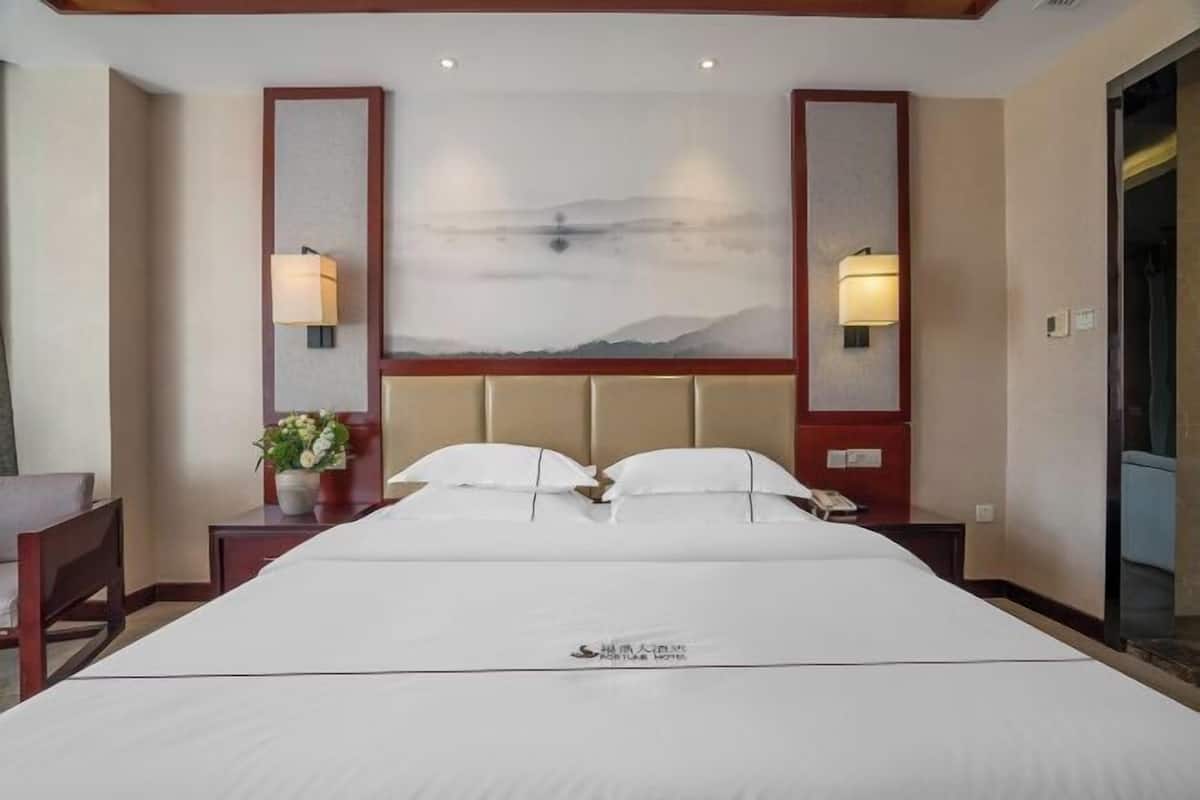 A hotel room with a large bed, two bedside lamps, a wall-mounted phone, and a decorative wall piece.
