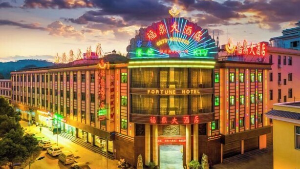 A multi-story hotel with a prominent neon sign and a large entrance. - Fortune Hotel (Luxi)
