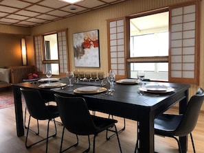 Un coin repas avec une table noire dressée pour quatre personnes, entourée de chaises noires, agrémenté d’une porte coulissante de style japonais traditionnel et d’un tableau accroché au mur.