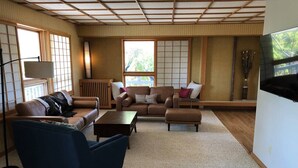 A living room with a sofa, armchair, and coffee table, a TV, and a large window with a view.