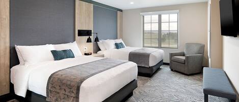 A hotel room with two beds, a chair, a bench, a TV, and a window with a view.