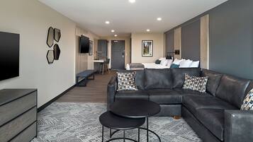 A modern living room with a sectional sofa, a small round table, and a TV mounted on the wall.