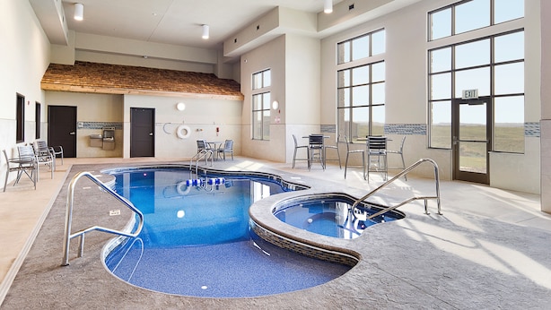 An indoor swimming pool with two separate sections, a tiled wall with a wooden ceiling, and a view of the outdoors through large windows.