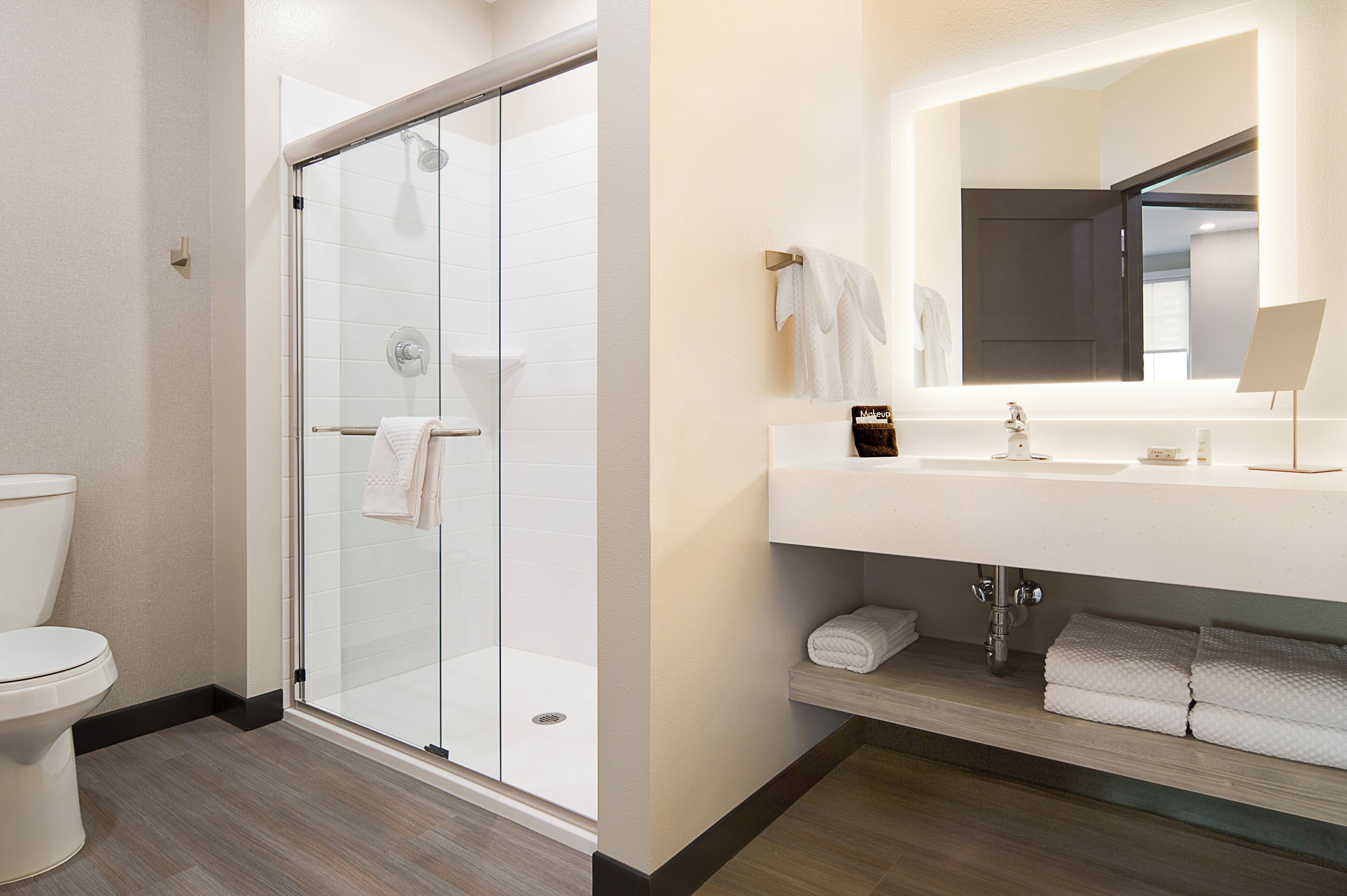 A modern bathroom with a glass-enclosed shower, a white sink with a mirror, and neatly folded towels.
