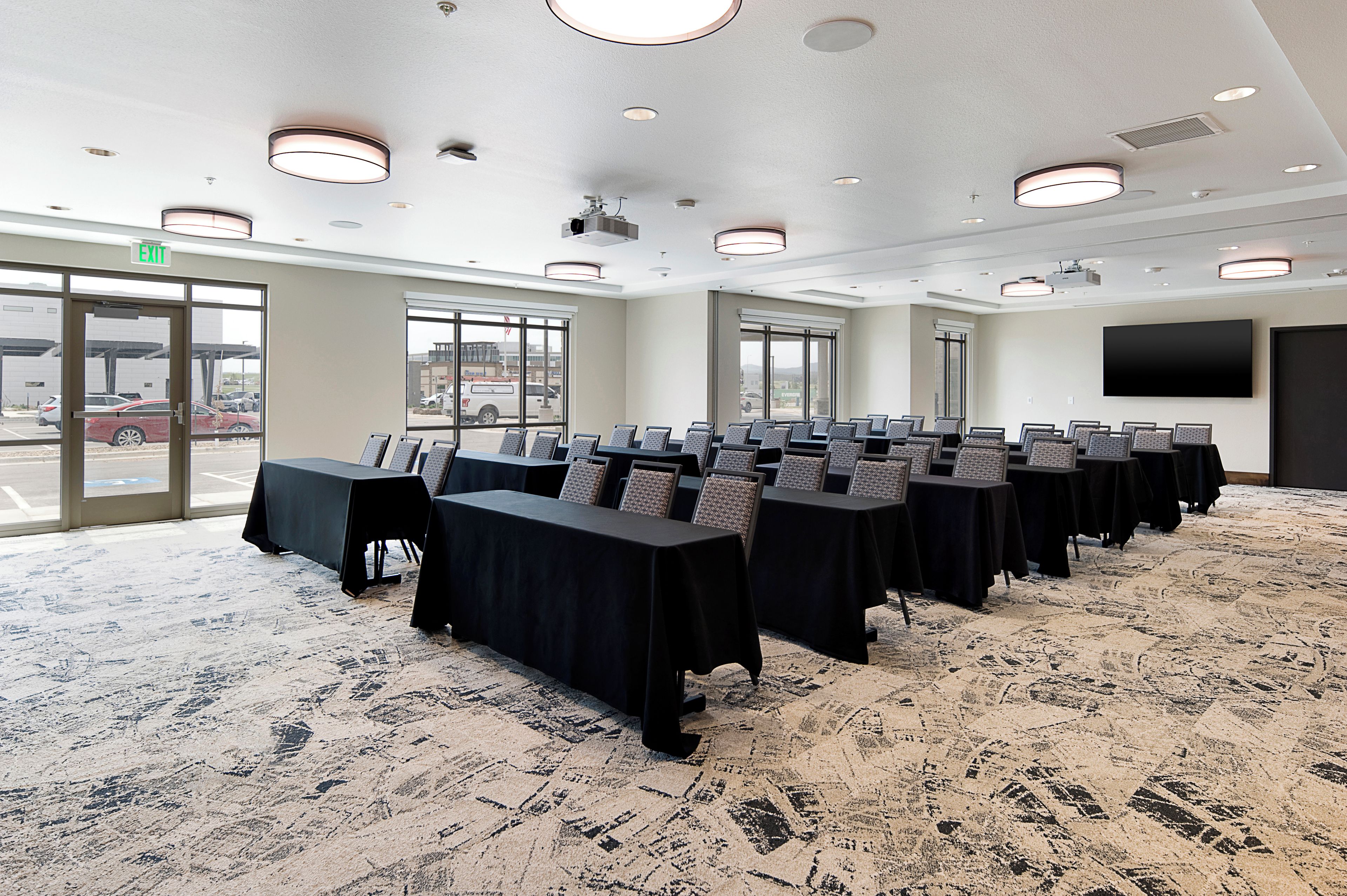 A conference room with multiple tables and chairs, large windows, and a carpeted floor.