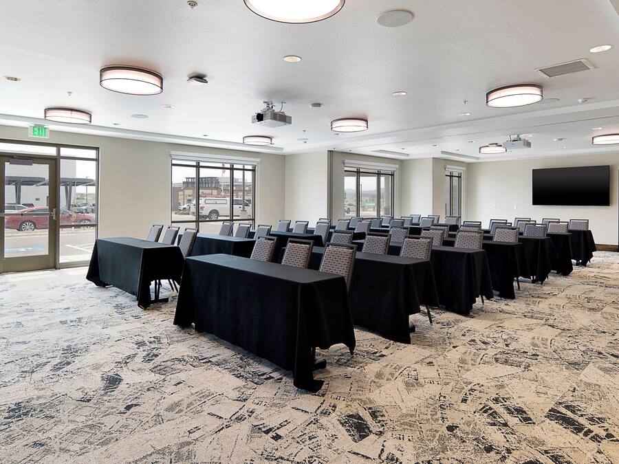A conference room with multiple tables and chairs, large windows, and a carpeted floor.