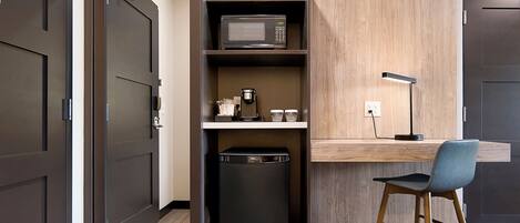 Una kitchenette compacta con microondas, cafetera y un pequeño cubo de basura.