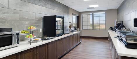 A modern kitchen with a microwave, stove, and refrigerator. There are fruit platters on the counter and a large window providing natural light.