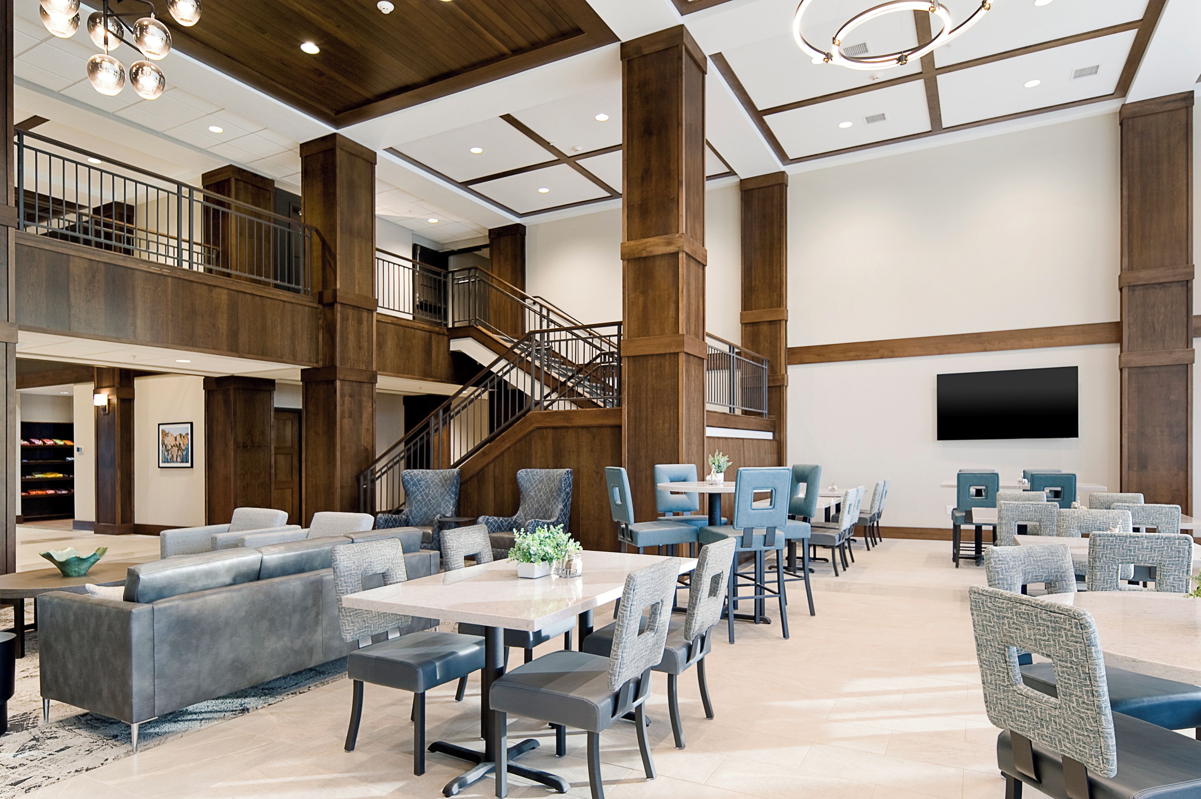 A spacious lobby with a staircase, seating areas, and a flat-screen TV mounted on the wall.