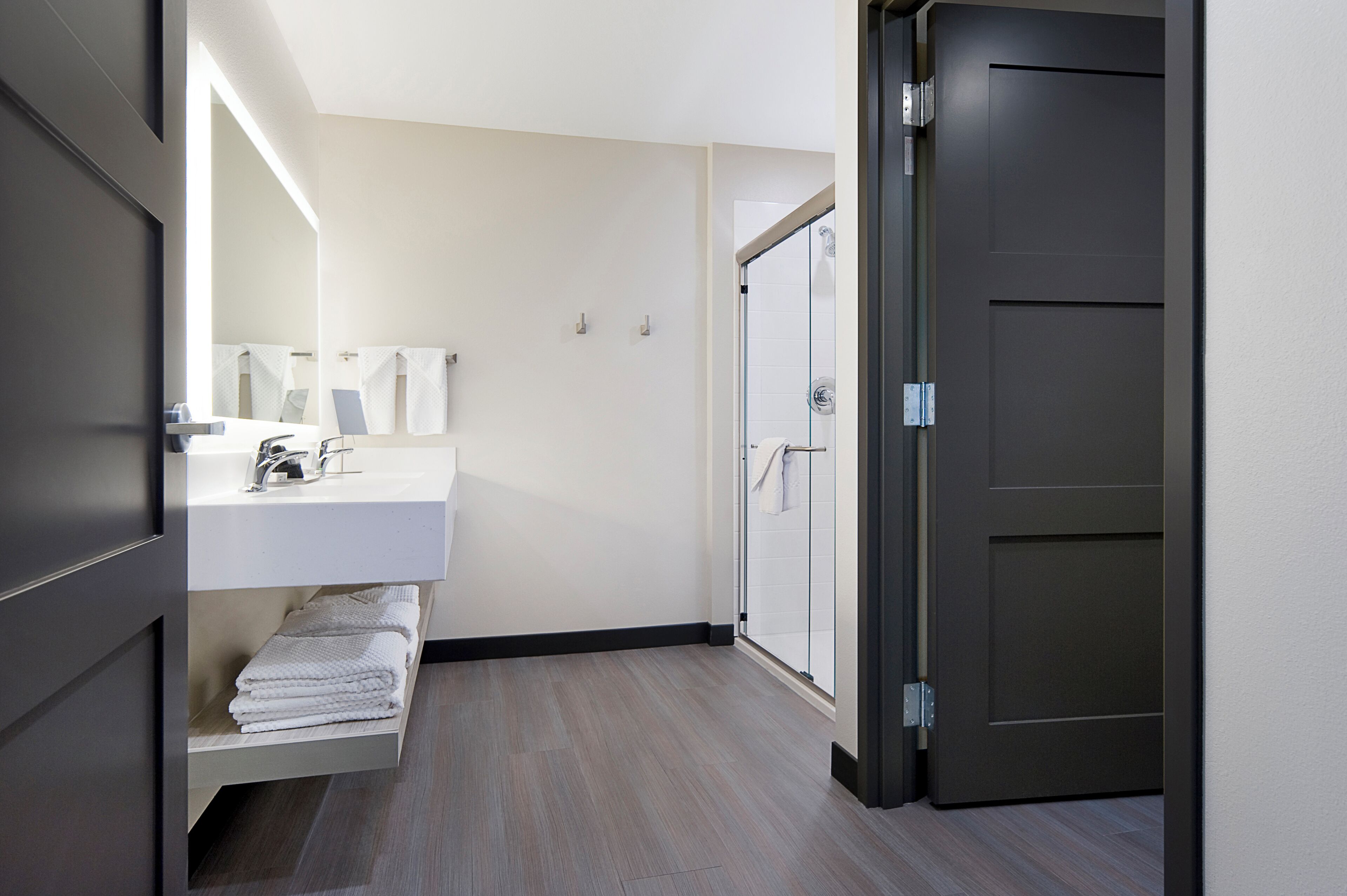 A modern bathroom with a white sink, towel rack, and a glass shower door.