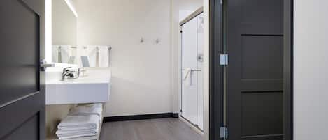 A modern bathroom with a white sink, towel rack, and a glass shower door.