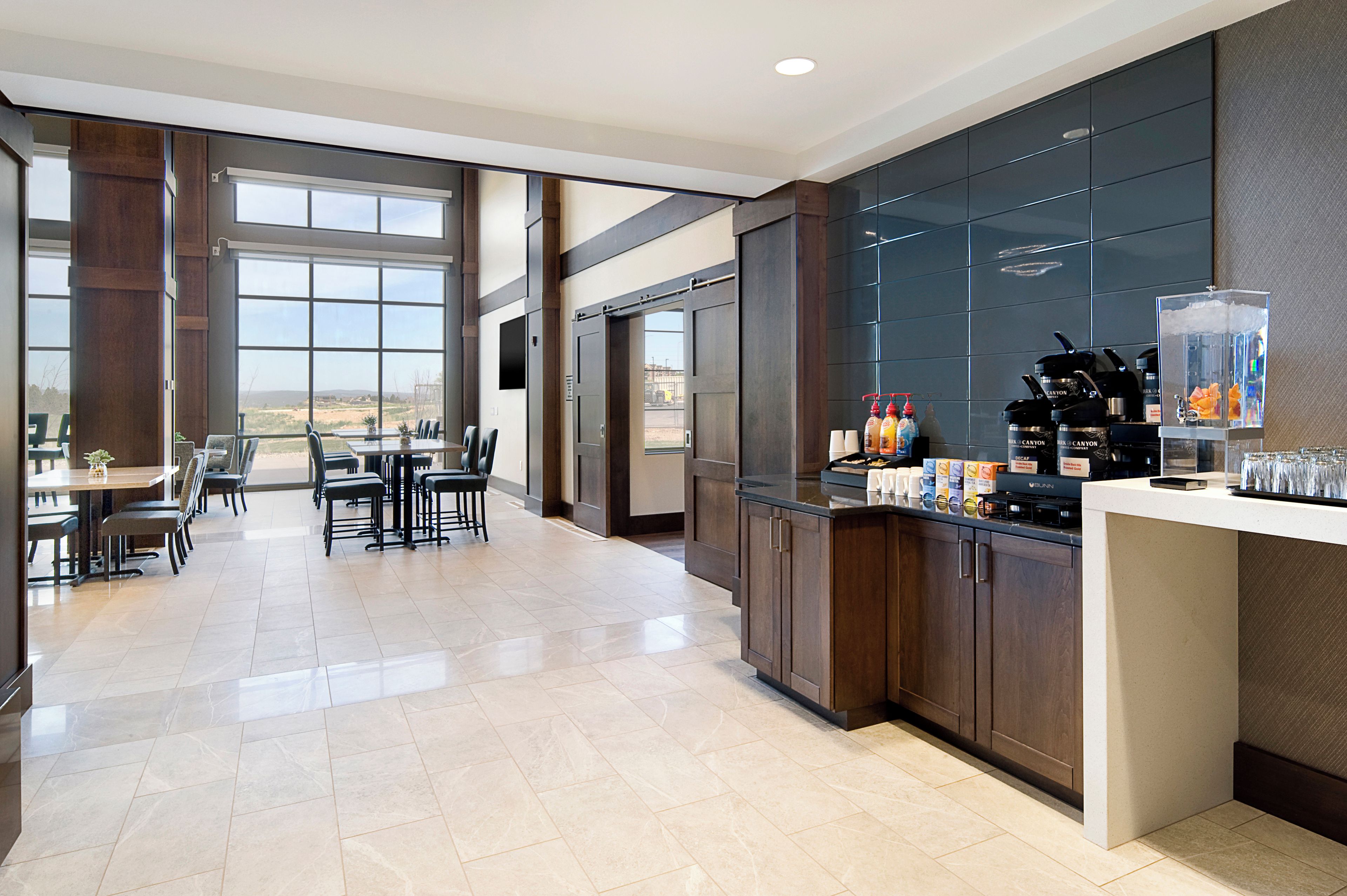 A modern kitchen with a bar area, large windows, and a dining area with chairs and tables.