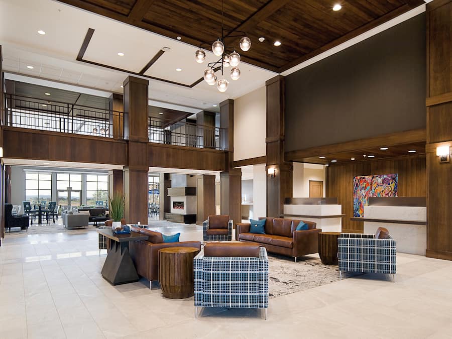 Eine großzügige Lobby mit hohen Decken, einer modernen Kronleuchter und einer Mischung verschiedener Sitzgelegenheiten, darunter Sofas und ein einzigartiger blau-weißer Sessel.