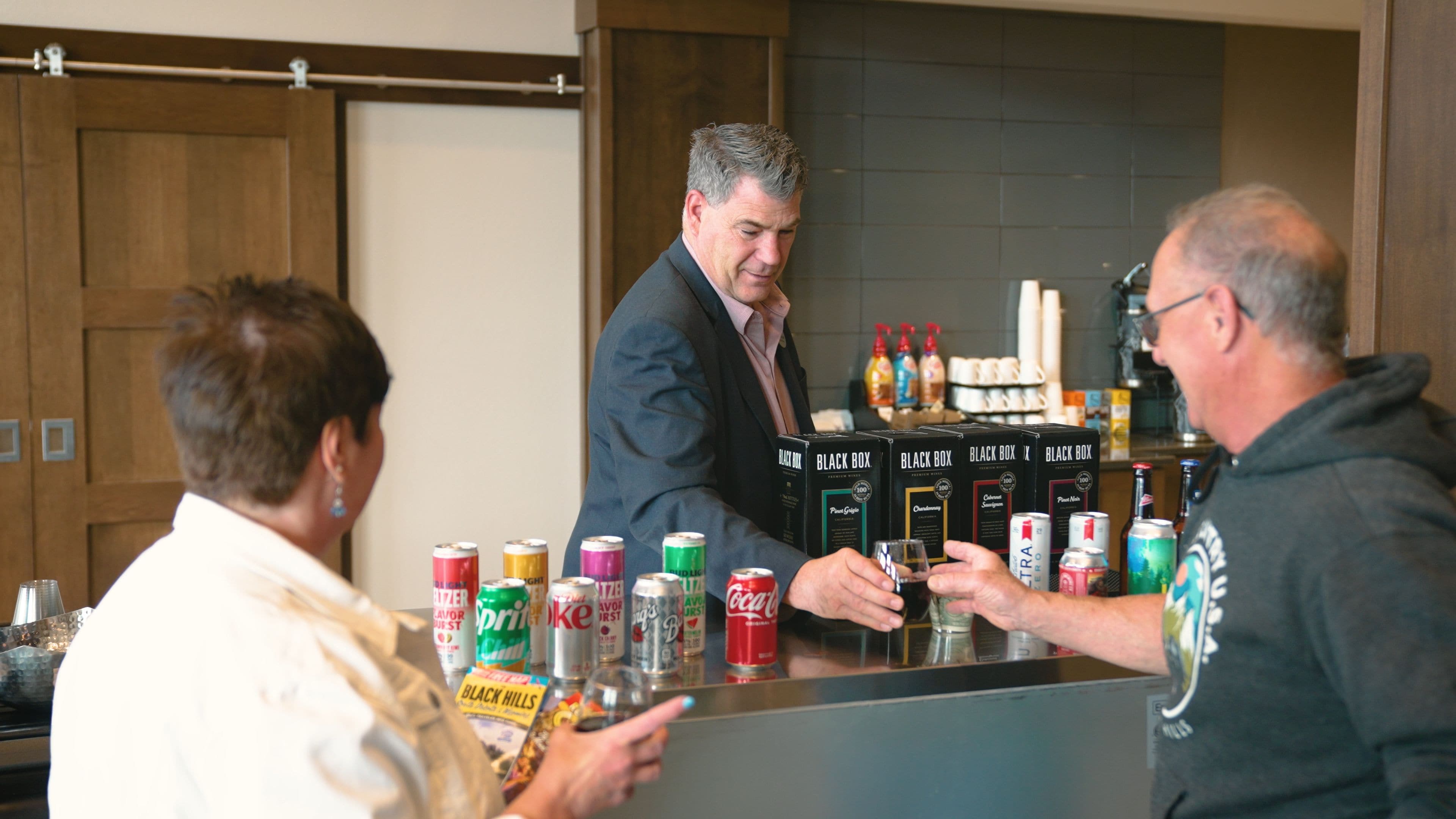 A bar area with a counter, various beverages, and a person behind the bar.
