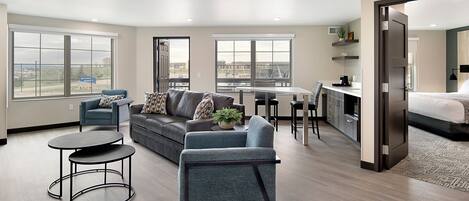 A modern apartment with a living room, dining area, and kitchenette. It features large windows, a sofa, a coffee table, and a bed.