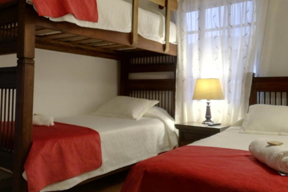 A room with two bunk beds, each with a red blanket, a wooden headboard, and a bedside table with a lamp.