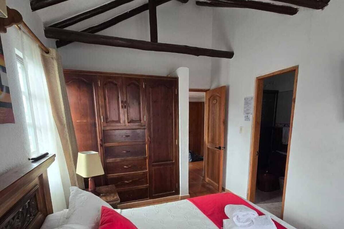 Un dormitorio con cama, armario de madera, cojín rojo y manta roja.