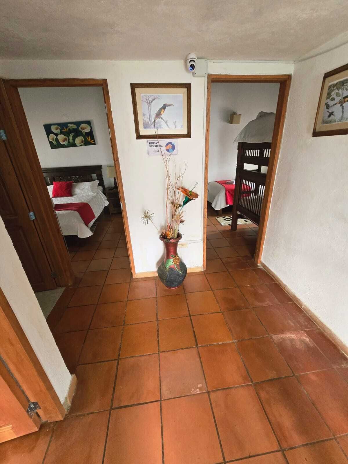 Un pasillo con suelo de baldosas, un marco de puerta de madera, una cama con almohada roja, un cuadro en la pared y un letrero que indica limpieza y desinfección.
