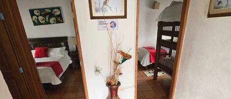Un pasillo con suelo de baldosas, un marco de puerta de madera, una cama con almohada roja, un cuadro en la pared y un letrero que indica limpieza y desinfección.