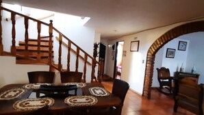 Un espace repas avec une table et des chaises en bois, un escalier et une arche en pierre menant à une autre pièce.
