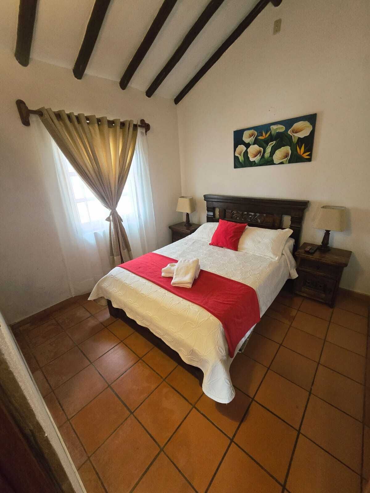Une chambre à coucher avec un lit, deux tables de chevet, une fenêtre avec des rideaux et un tableau au mur.
